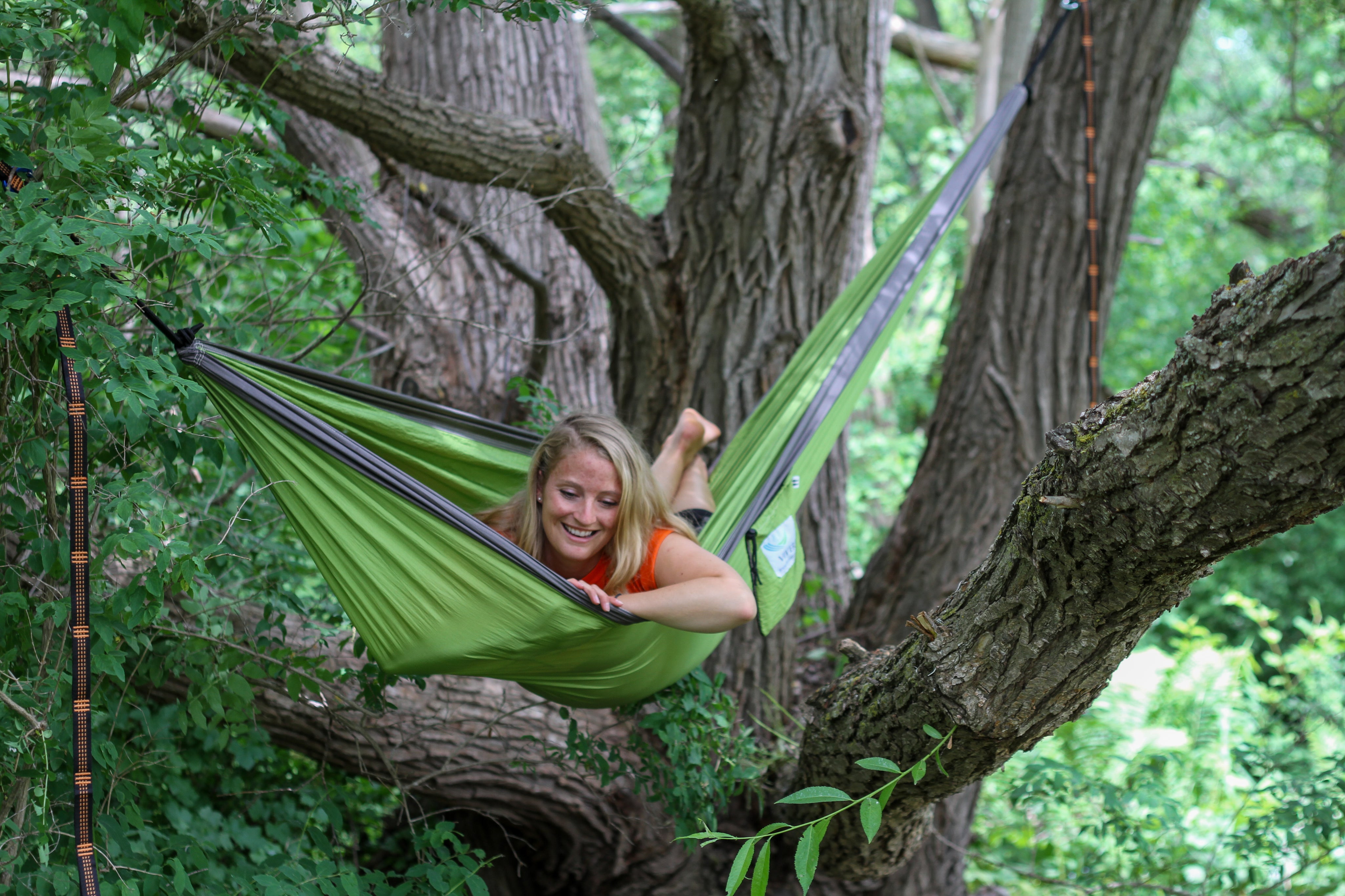 Woman hanging in green Vivere parachute camping hammock outdoors in a tree 