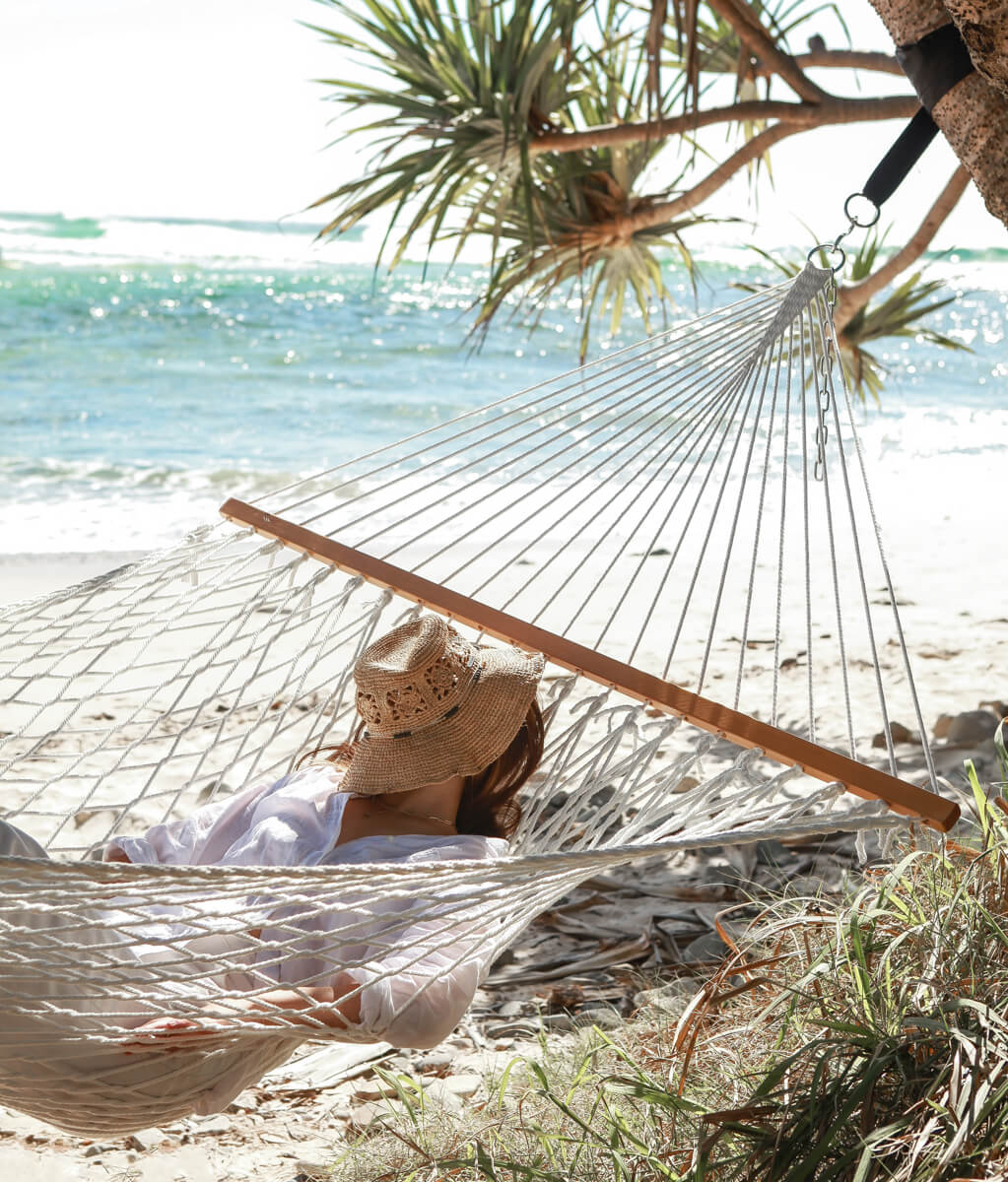Person relaxing in a hammock on a beach with palm trees and ocean view